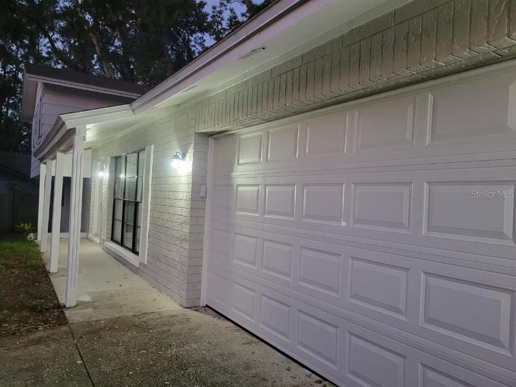 A white brick house exterior features a garage door, a covered porch, and exterior lighting — 3610 GREENSTONE PLACE, VALRICO, FL