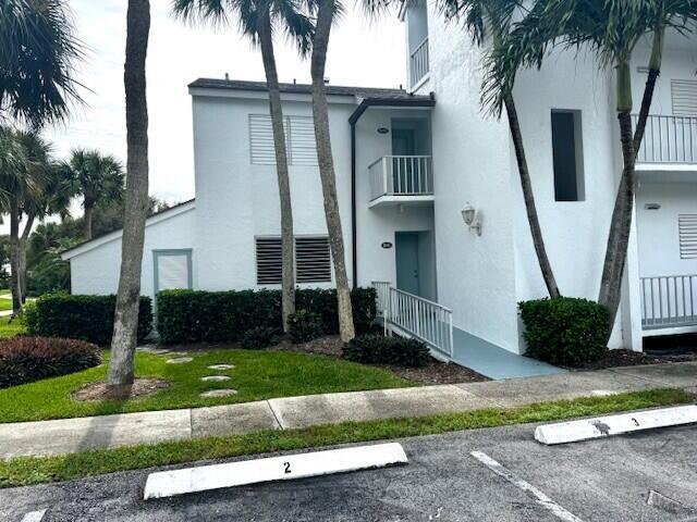 A white two-story apartment building features palm trees, a wheelchair ramp, and numbered parking spaces — 1550 NE Ocean Boulevard # B101, Stuart FL 34996, STUART, FL