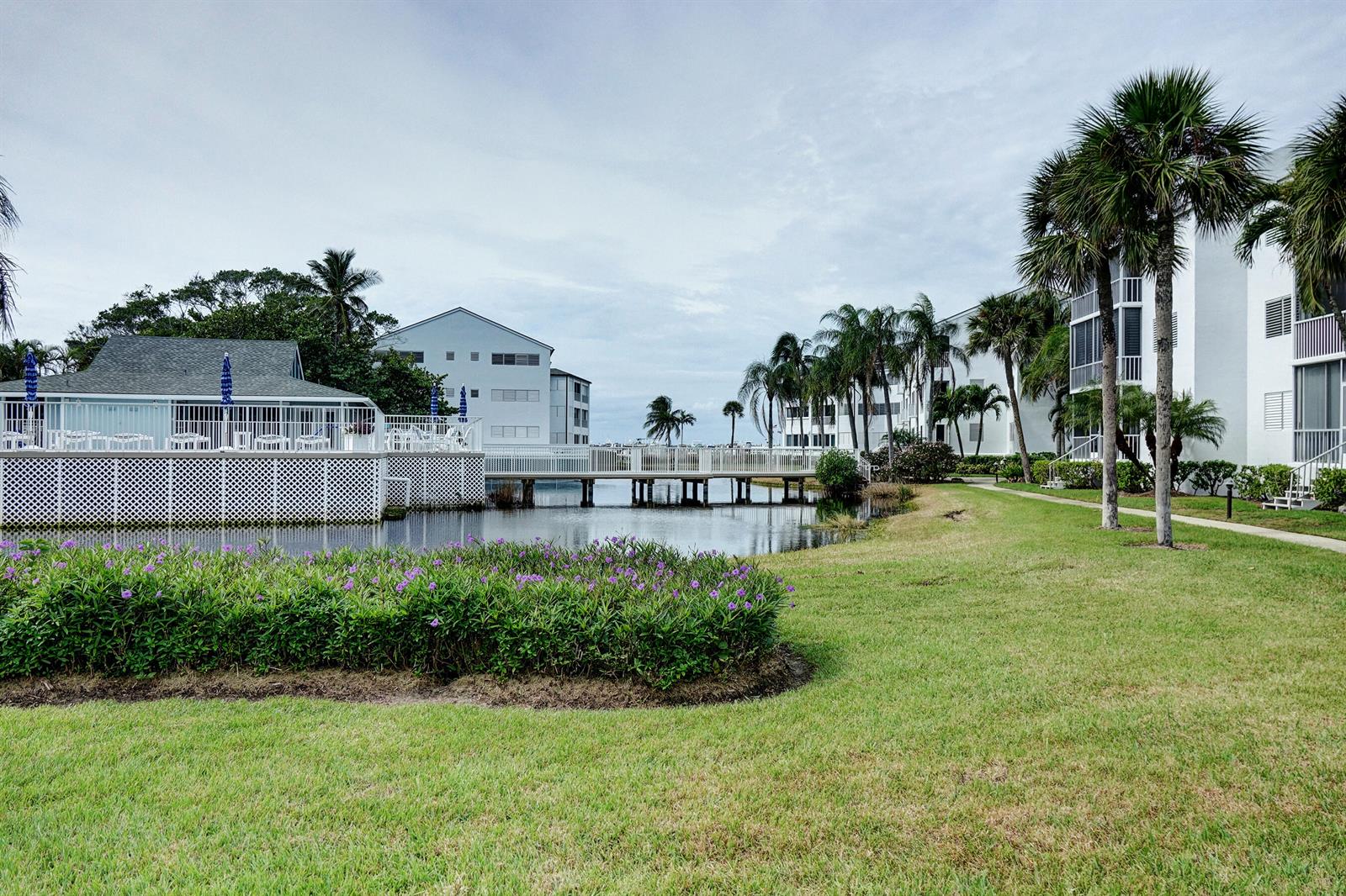 A grassy lawn with purple flowers leads to a white building and a pedestrian bridge — 1550 NE Ocean Boulevard # B101, Stuart FL 34996, STUART, FL