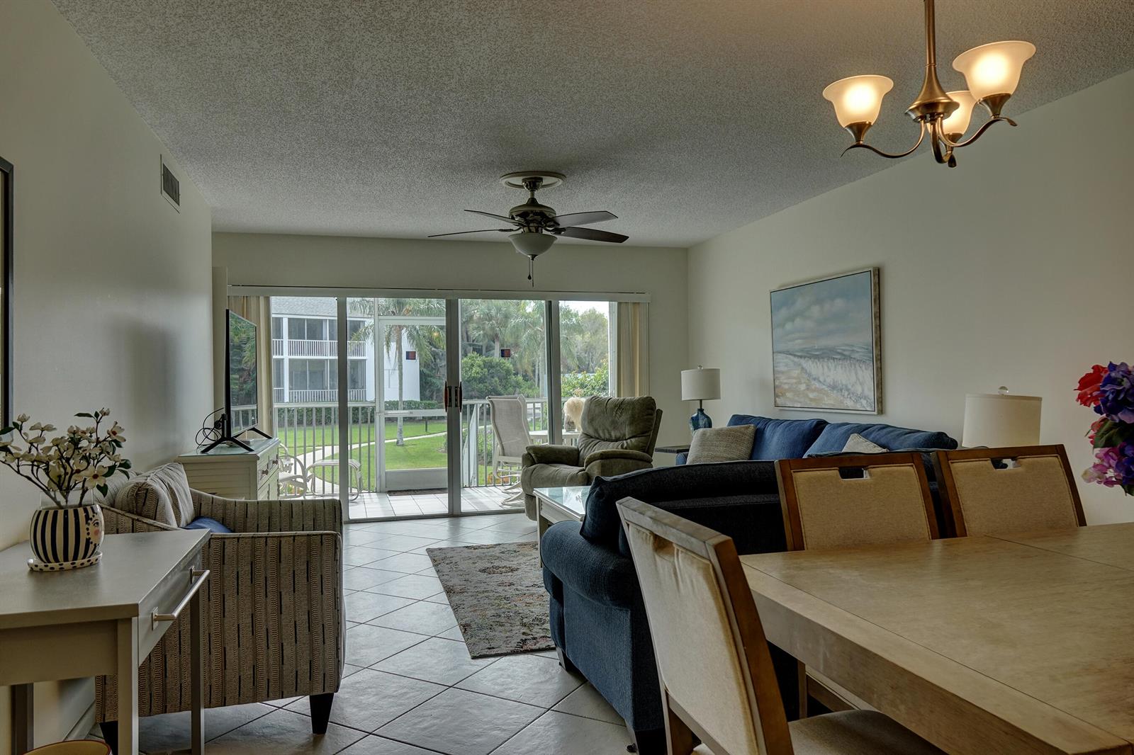 A living and dining area with tile floors, a blue sofa, and a sliding glass door — 1550 NE Ocean Boulevard # B101, Stuart FL 34996, STUART, FL
