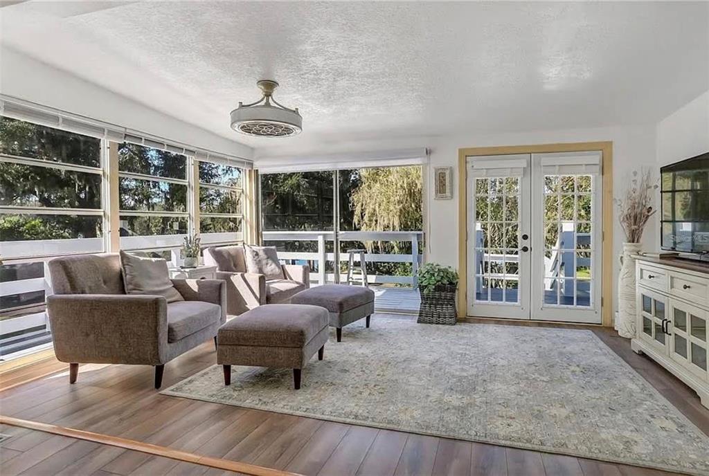 A sunroom features wood-look flooring, gray armchairs with ottomans, and French doors leading to a deck — 1192 ERROL PARKWAY, APOPKA, FL