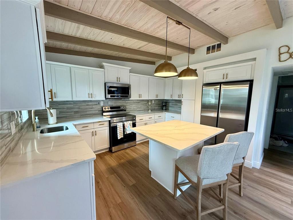 A kitchen features white cabinets, a stone island, stainless steel appliances, and a wood-beamed ceiling — 1209 S CENTRAL AVENUE, FLAGLER BEACH, FL