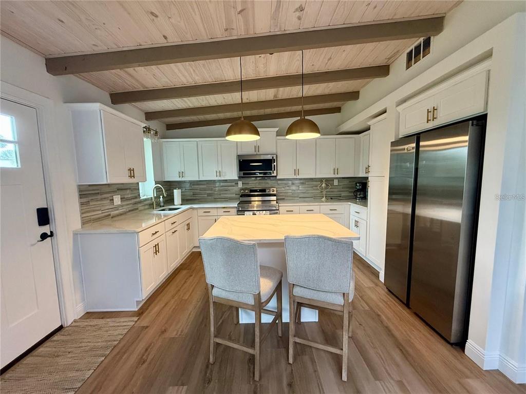 A kitchen features white cabinets, a central island with two chairs, and wood-paneled ceiling beams — 1209 S CENTRAL AVENUE, FLAGLER BEACH, FL