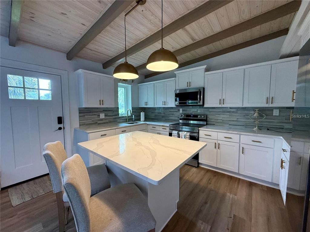 A kitchen features white cabinetry, a quartz island, pendant lighting, and a wood-paneled ceiling — 1209 S CENTRAL AVENUE, FLAGLER BEACH, FL