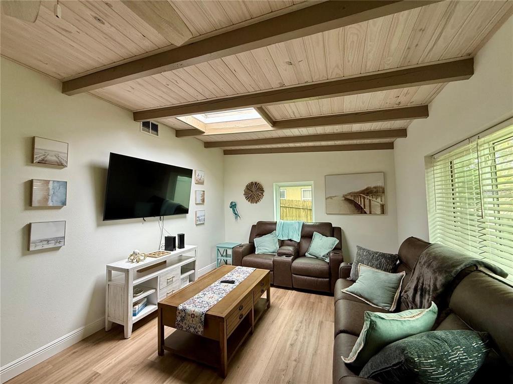 A living room features a vaulted wood-plank ceiling with beams, a skylight, and brown furniture — 1209 S CENTRAL AVENUE, FLAGLER BEACH, FL