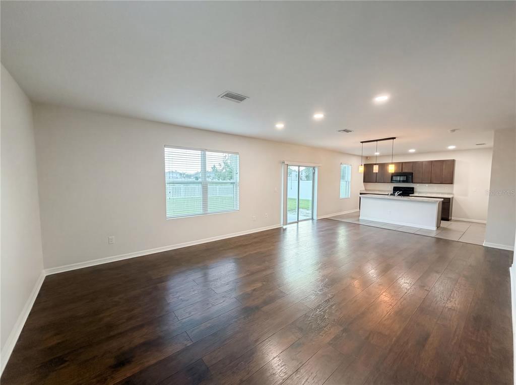 An open-concept living area features dark wood flooring, a kitchen with an island, and sliding doors — 35687 HILLBROOK AVENUE, ZEPHYRHILLS, FL