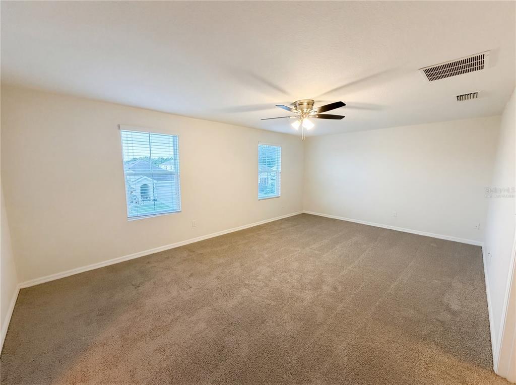 A spacious, empty bedroom features beige carpet, cream-colored walls, two windows, and a ceiling fan — 35687 HILLBROOK AVENUE, ZEPHYRHILLS, FL