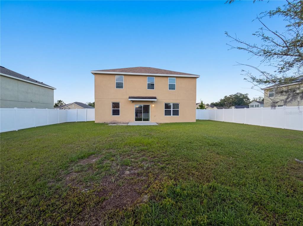 The rear exterior of a two-story beige house features a fenced backyard and lawn — 35687 HILLBROOK AVENUE, ZEPHYRHILLS, FL
