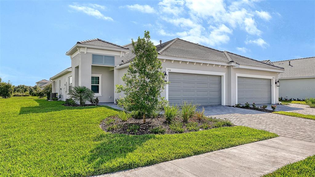 A single-story house with a three-car garage and a paved driveway under a blue sky — 2316 BLUE MAHOE LANE, SARASOTA, FL