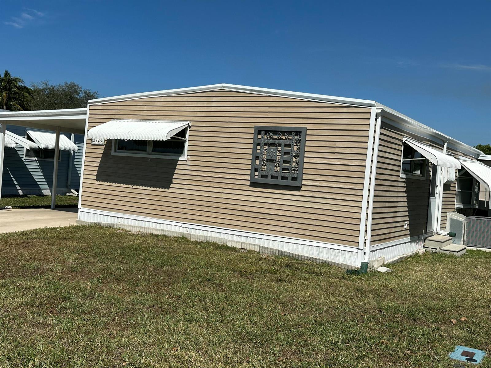 A tan mobile home with white trim, awnings, and a decorative metal wall panel — 8349 South Street, Boca Raton FL 33433, BOCA RATON, FL