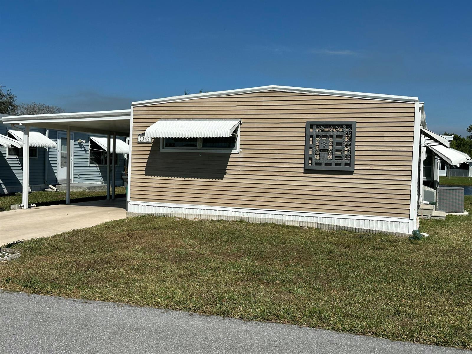 A tan mobile home with a carport, white awnings, and a decorative square window panel — 8349 South Street, Boca Raton FL 33433, BOCA RATON, FL
