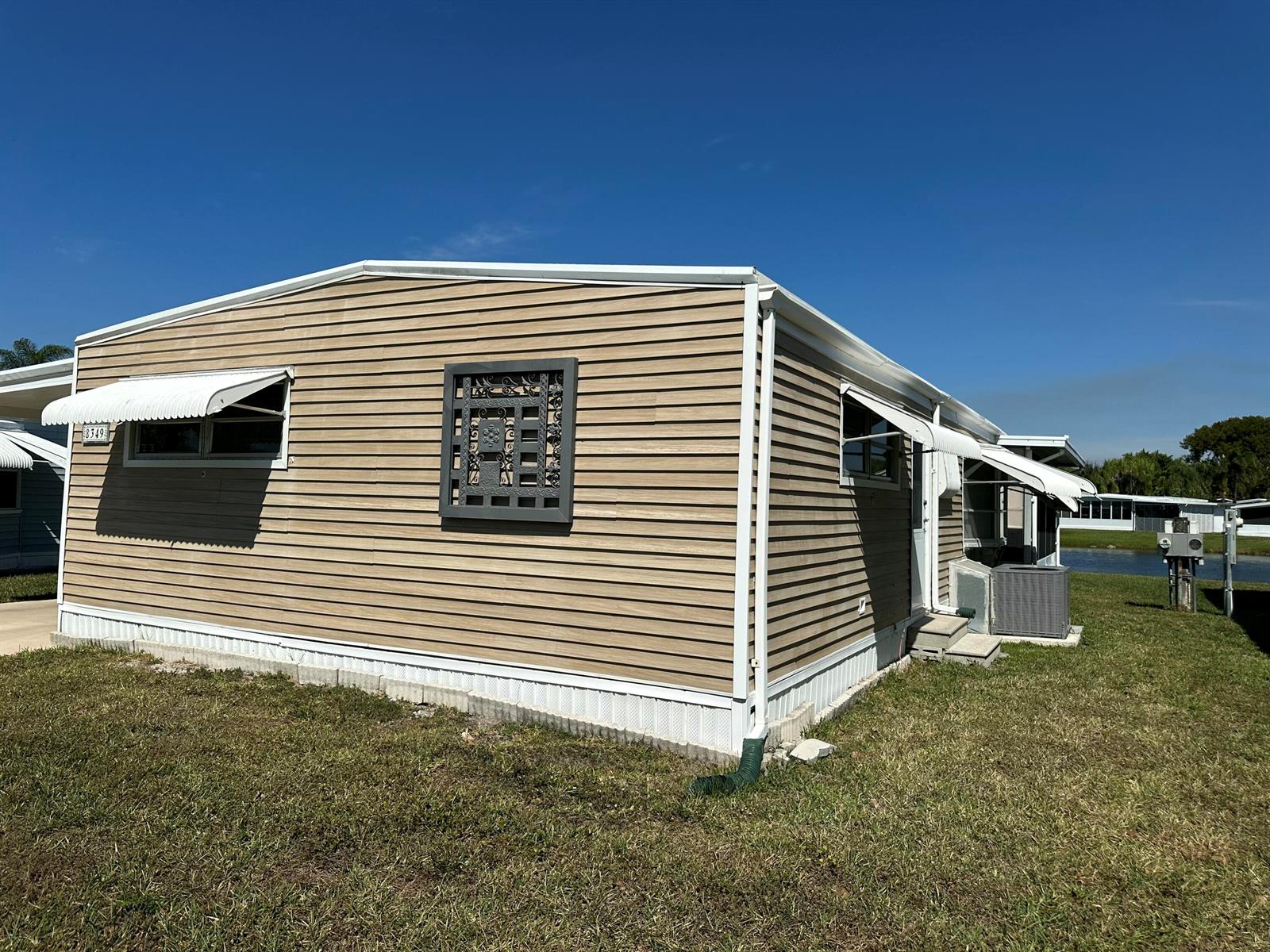 A tan mobile home with horizontal siding, white trim, and window awnings sits on grass — 8349 South Street, Boca Raton FL 33433, BOCA RATON, FL