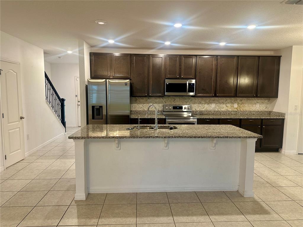 A kitchen featuring dark wood cabinets, granite countertops, a central island, and stainless steel appliances — 125 VILLAVISTA COURT, DAVENPORT, FL