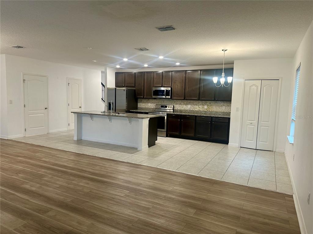 A kitchen with dark wood cabinets, granite countertops, and a white island overlooks a living area — 125 VILLAVISTA COURT, DAVENPORT, FL