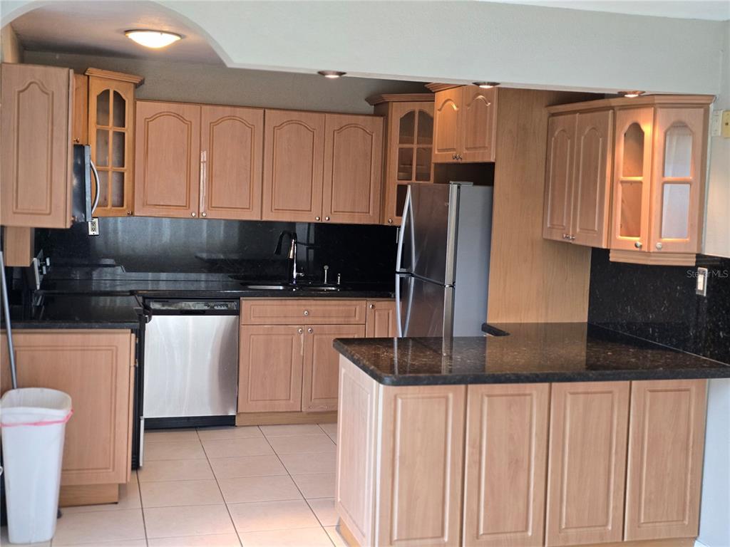 A kitchen with light wood cabinets, black countertops, stainless steel appliances, and beige tile flooring — 2913 MCINTOSH ROAD, SARASOTA, FL