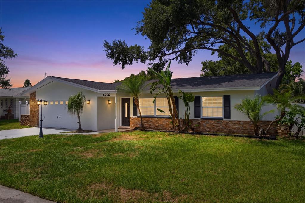 A single-story house with white siding, stone accents, and a garage at dusk — 1656 WEBB DRIVE, CLEARWATER, FL