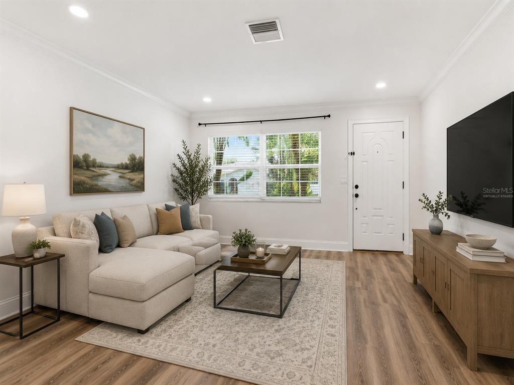 A living room features a sectional sofa, coffee table, media console, and light wood flooring — 1656 WEBB DRIVE, CLEARWATER, FL