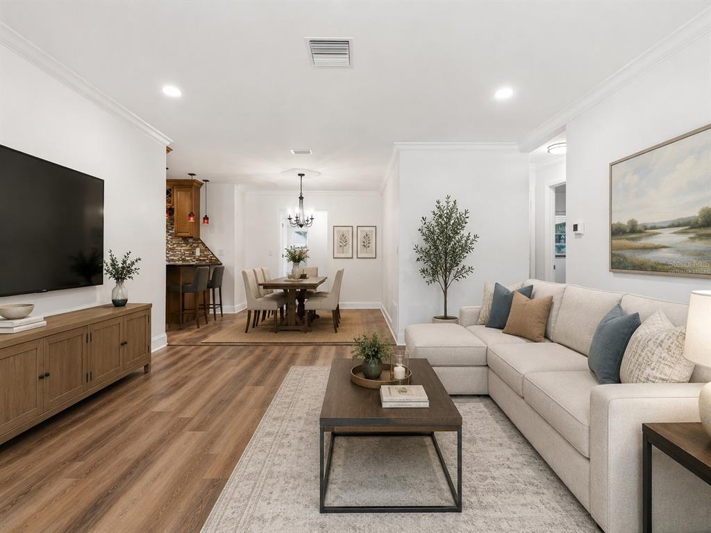 An open-concept living and dining area features wood-look flooring, a sectional sofa, and kitchen bar — 1656 WEBB DRIVE, CLEARWATER, FL