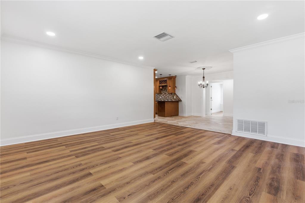 A spacious living area with wood-look flooring transitions into a kitchen with wooden cabinets — 1656 WEBB DRIVE, CLEARWATER, FL
