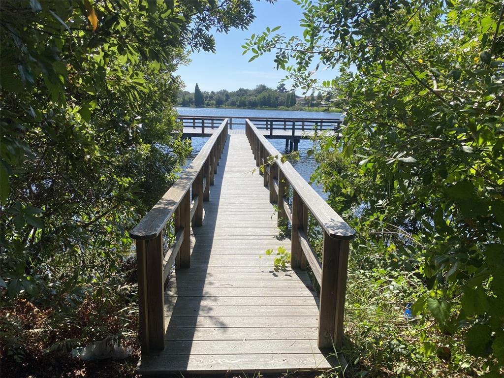 A wooden dock with railings extends through trees toward a lake under a clear sky — 10422 LAKE MONTAUK DRIVE, RIVERVIEW, FL