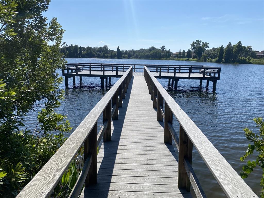 A wooden pier with railings extends over a calm lake under a clear blue sky — 10422 LAKE MONTAUK DRIVE, RIVERVIEW, FL