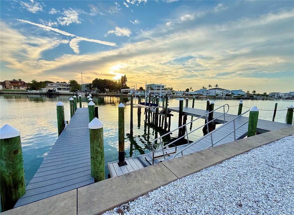 A wooden dock with white-capped pilings extends into a calm bay at sunset — 2216 DONATO DRIVE, BELLEAIR BEACH, FL