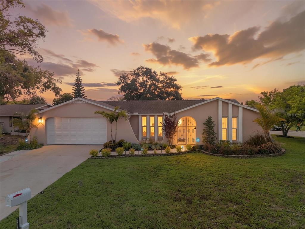 A single-story house with a white garage door and arched entryway at sunset — 7312 VIENNA LANE, PORT RICHEY, FL