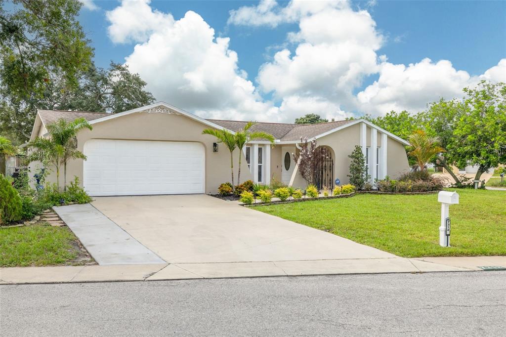A single-story house with a white garage door, beige stucco exterior, and a front lawn — 7312 VIENNA LANE, PORT RICHEY, FL
