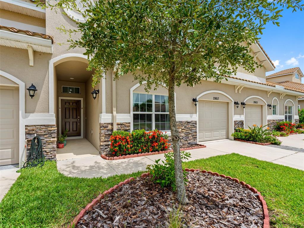 A beige townhouse exterior features a stone-accented facade, a front door, and two garage doors — 29817 GANGA WAY, WESLEY CHAPEL, FL