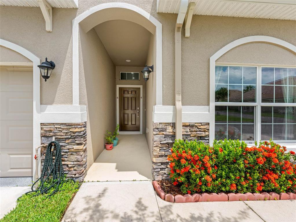 The exterior of a home features a covered entryway, stone accents, and a landscaped garden — 29817 GANGA WAY, WESLEY CHAPEL, FL