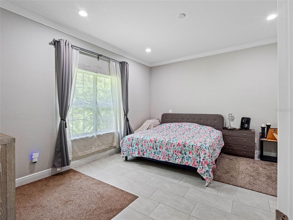 A bedroom features light gray walls, tile flooring, two area rugs, and a floral bedspread — 29817 GANGA WAY, WESLEY CHAPEL, FL