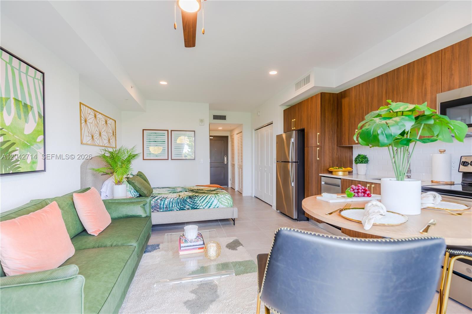 A studio apartment features a green sofa, a bed, and a kitchen with wood cabinets — 1005 Spring Garden Rd # 433, Miami FL 33136, MIAMI, FL