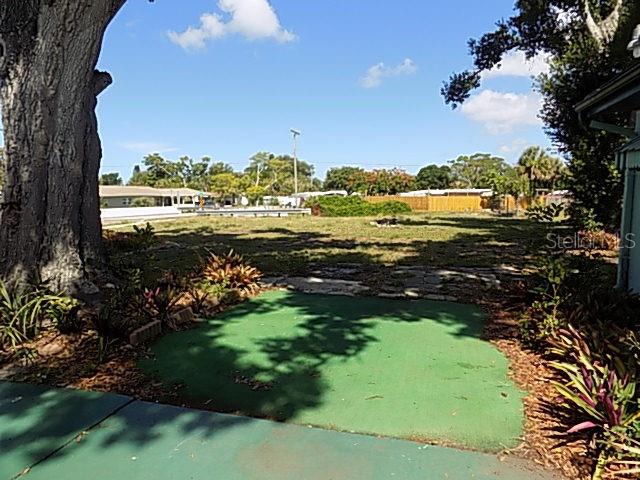 A large, grassy vacant lot is viewed from a shaded patio area with green flooring — 1000 DARTMOUTH DRIVE, BRADENTON, FL