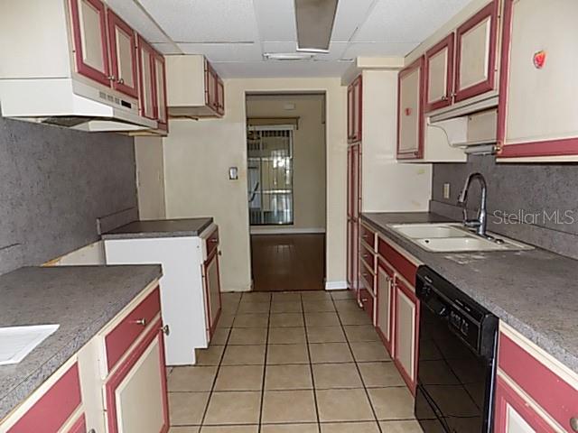 A galley kitchen features two-toned cabinets, gray countertops, a black dishwasher, and tiled flooring — 1000 DARTMOUTH DRIVE, BRADENTON, FL