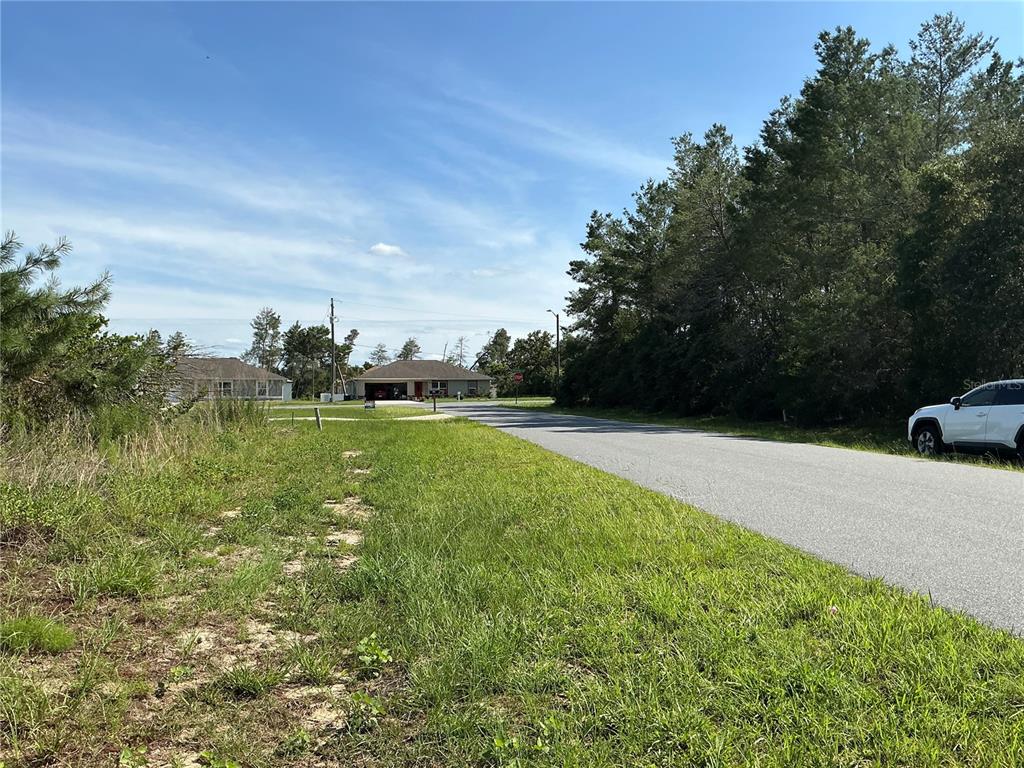 A paved road leads past a grassy lot toward a suburban house under a blue sky — TBD SW 35TH AVENUE ROAD, OCALA, FL