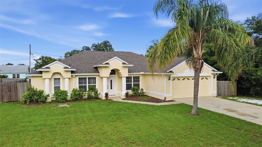 A single-story yellow house with a two-car garage and a palm tree in the yard — 521 TACOMA AVENUE, DELTONA, FL