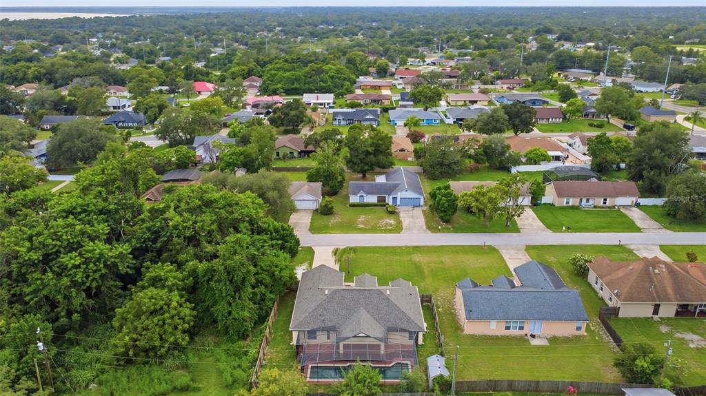 An aerial view shows a suburban neighborhood with houses, green lawns, and dense trees — 521 TACOMA AVENUE, DELTONA, FL