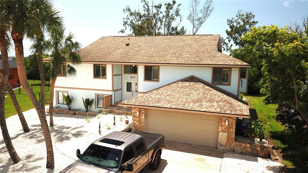 An elevated exterior view of a two-story house with a garage and palm trees — 607 IXORA AVENUE, ELLENTON, FL