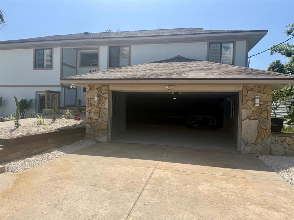 A two-story house features a stone-accented garage and a concrete driveway under a clear sky — 607 IXORA AVENUE, ELLENTON, FL