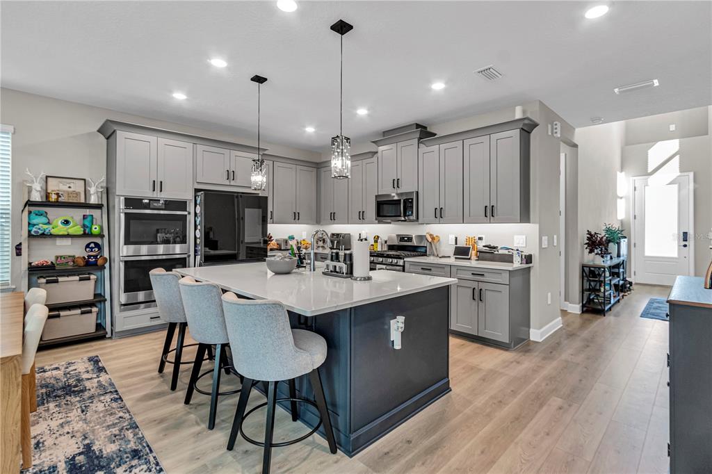 A modern kitchen features gray cabinetry, a large central island, and light wood flooring — 16271 HONEY HARVEST STREET, WINTER GARDEN, FL