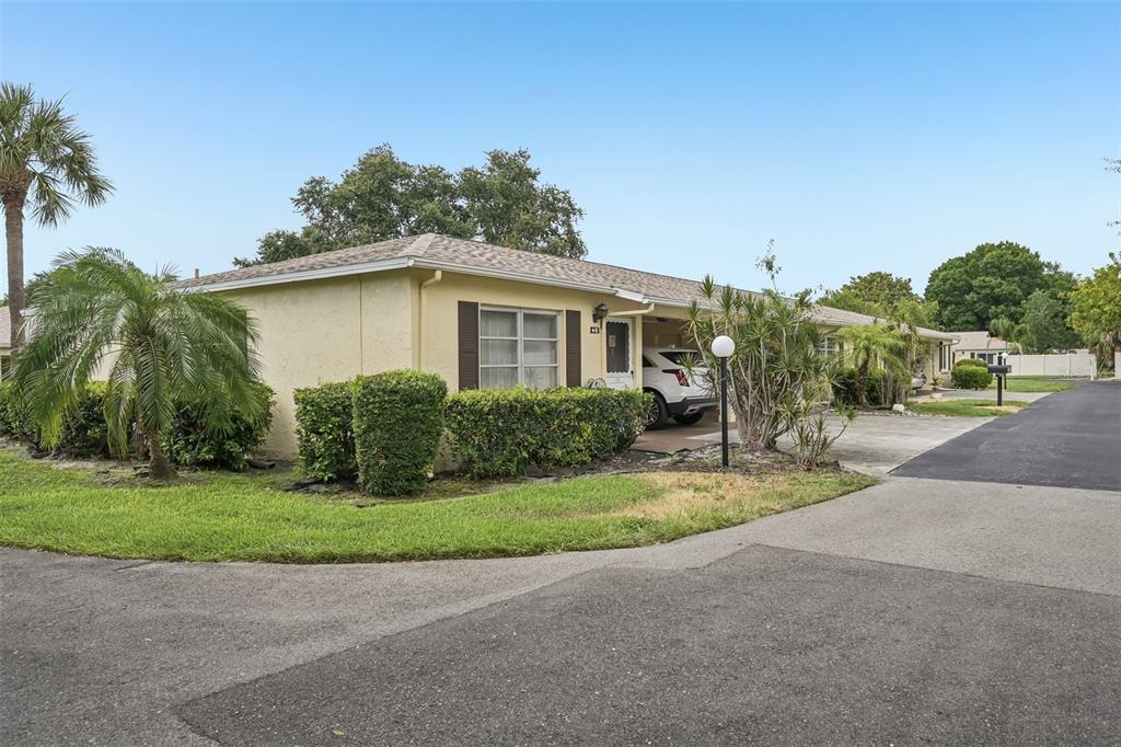 A single-story yellow stucco duplex with a carport and landscaped front yard — 390 301 BOULEVARD W UNIT 4D, BRADENTON, FL