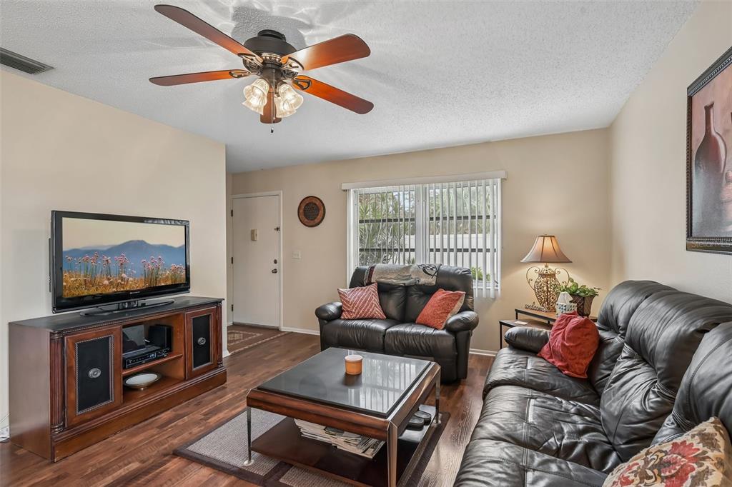 A living room features a ceiling fan, dark leather sofas, a television, and wood flooring — 390 301 BOULEVARD W UNIT 4D, BRADENTON, FL