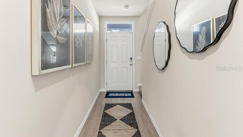 A narrow entryway features light wood flooring, framed wall art, and two decorative mirrors — 7616 42ND LANE N, PINELLAS PARK, FL
