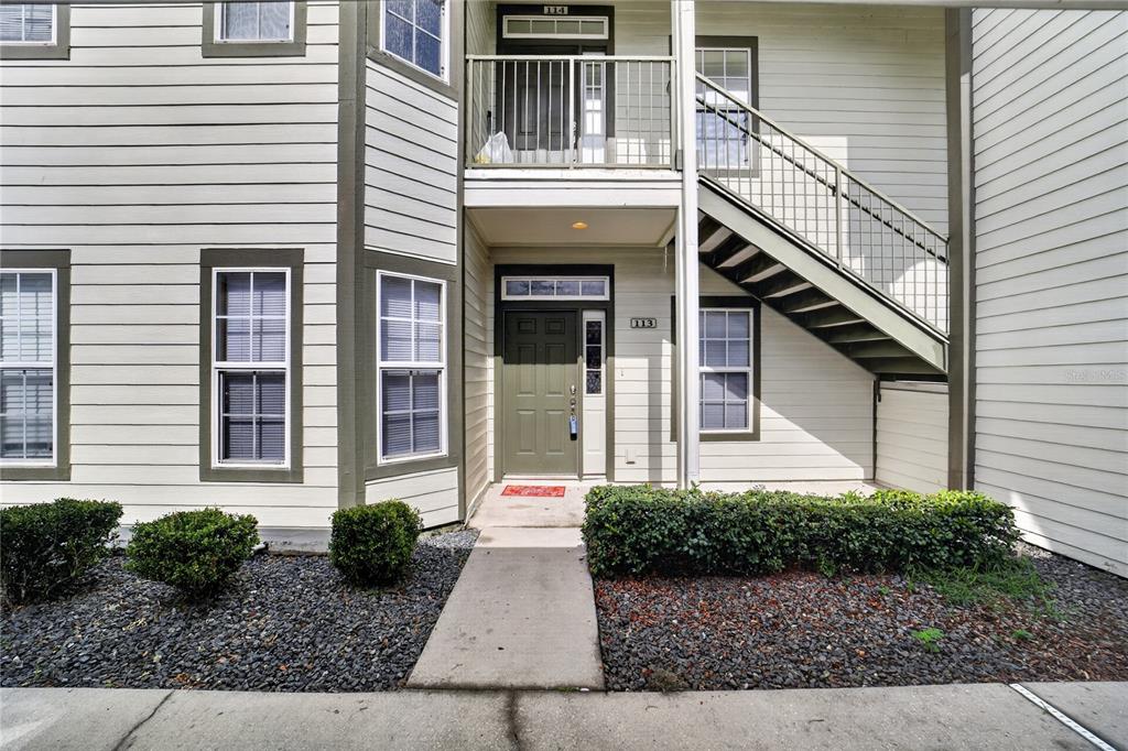 A two-story apartment building exterior features a ground-level entrance, an upper balcony, and metal stairs — 2935 NE 7TH STREET UNIT 113, OCALA, FL