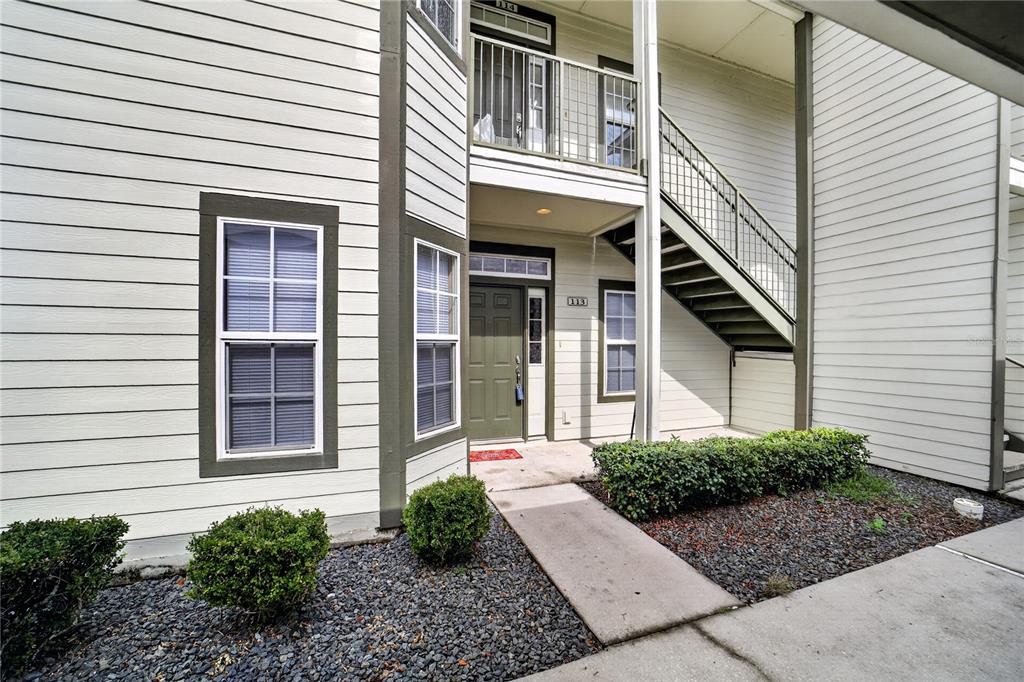 The exterior view shows a two-story apartment building with beige siding, a green door, and stairs — 2935 NE 7TH STREET UNIT 113, OCALA, FL