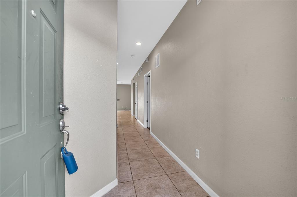 A hallway with tan tile flooring leads from an open door toward a living area — 2935 NE 7TH STREET UNIT 113, OCALA, FL