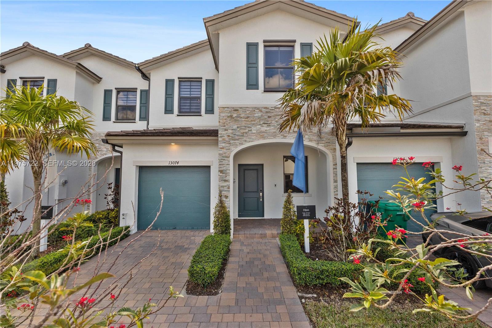 A two-story townhouse features a stone facade, a paved driveway, and a blue garage door — 13074 SW 233rd Ter, Homestead FL 33032, HOMESTEAD, FL
