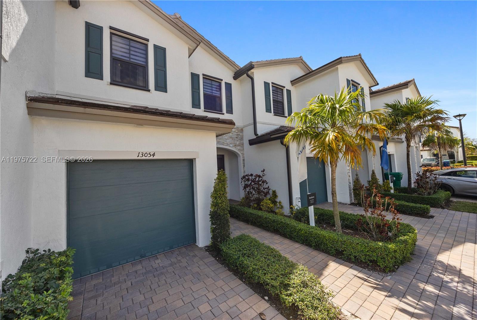 A row of two-story townhomes features white stucco exteriors, dark green garage doors, and paved driveways — 13074 SW 233rd Ter, Homestead FL 33032, HOMESTEAD, FL