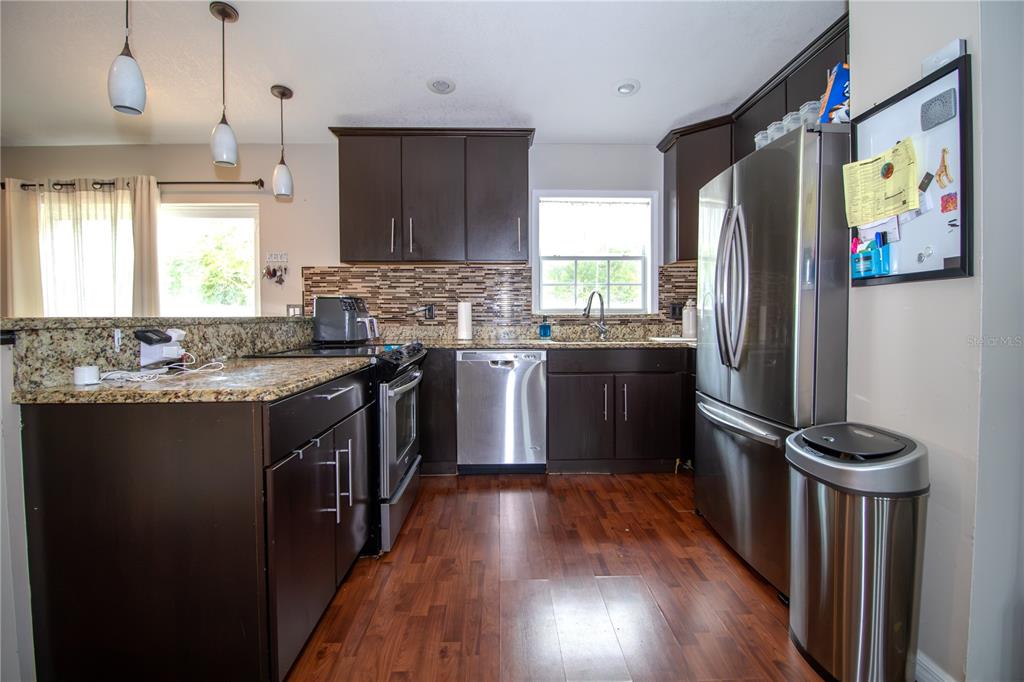 A kitchen features dark wood cabinets, granite countertops, stainless steel appliances, and wood-look flooring — 103 CASHEW COURT, LONGWOOD, FL