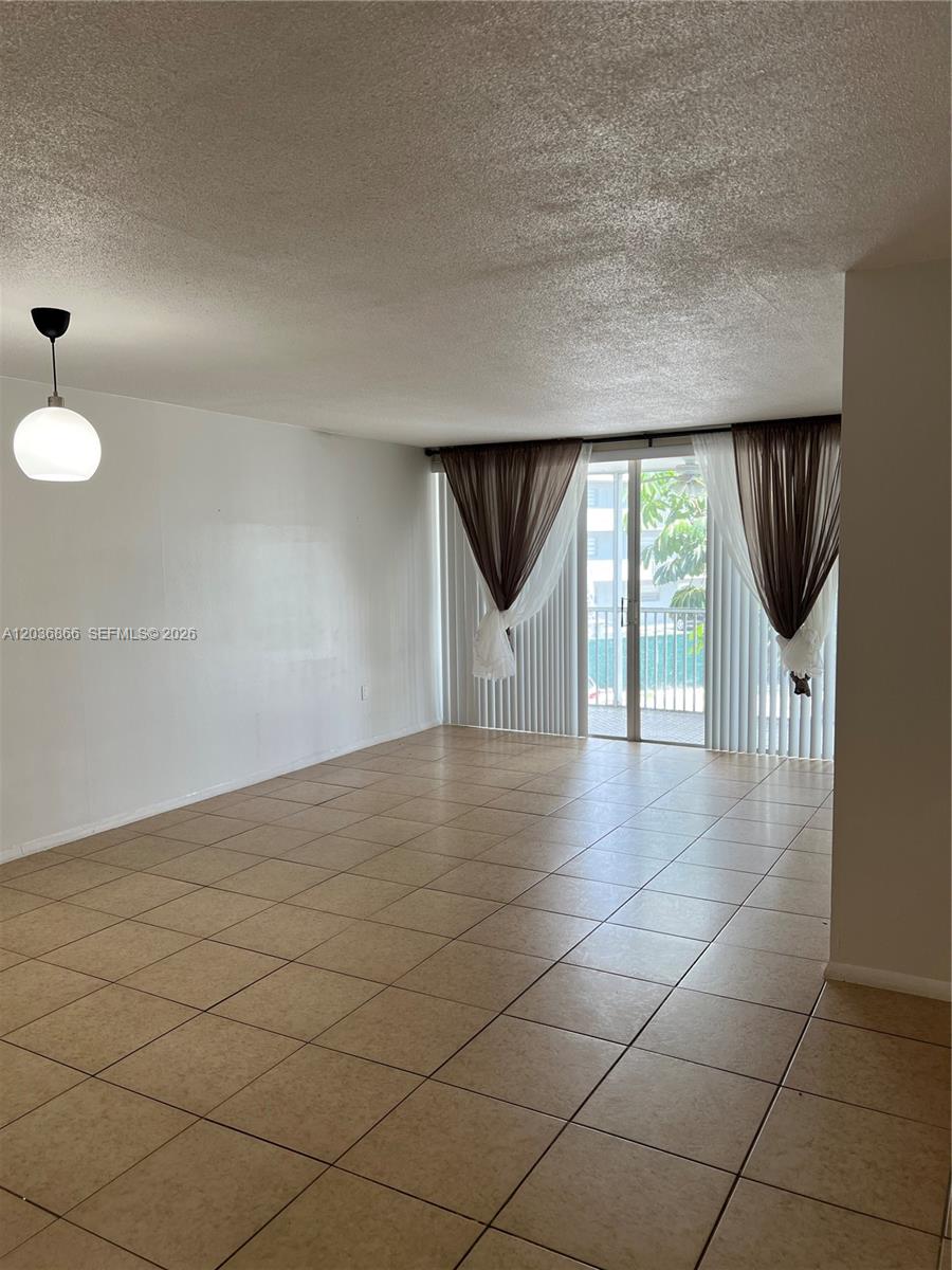 An empty living room features beige tile flooring, white walls, and a sliding glass door — 1680 NE 191st St # 2, Miami FL 33179, MIAMI, FL